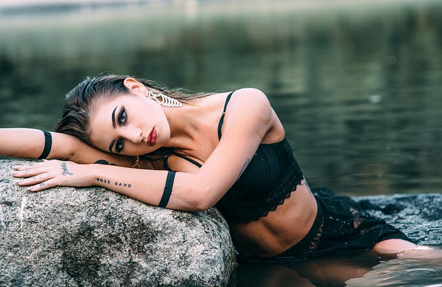 Krásna žena s tetovaním sedí vo vode pri skale.jpg