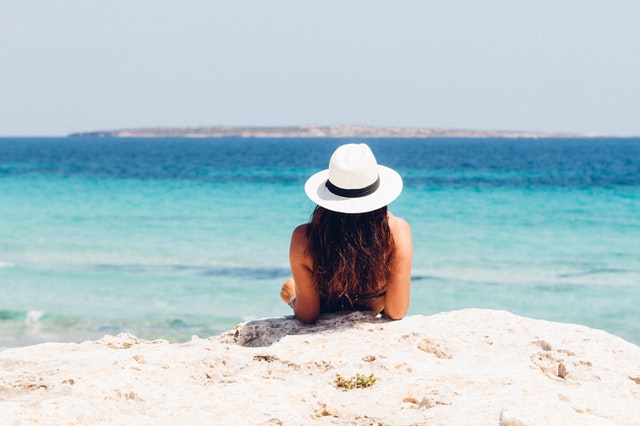 Žena v plavkách a bielom klobúku leží na pláži 