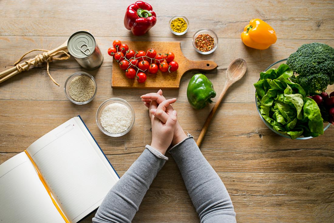 woman-leaning-on-table-with-various-ingredients-and-a-diet-planning-book